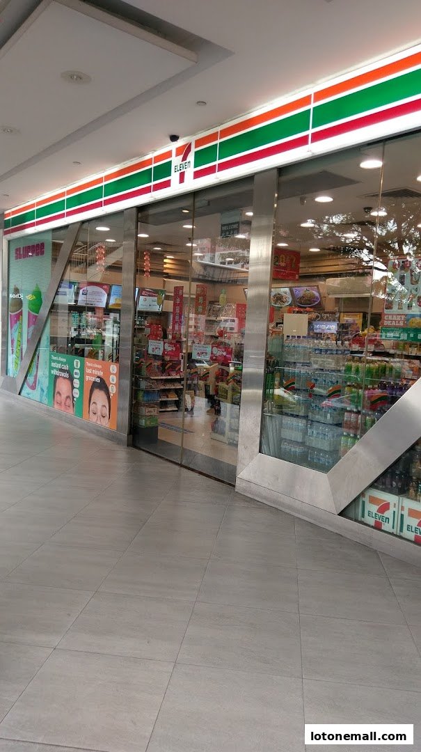 The exterior of a brightly lit 7-Eleven convenience store with glass doors and windows displaying products.