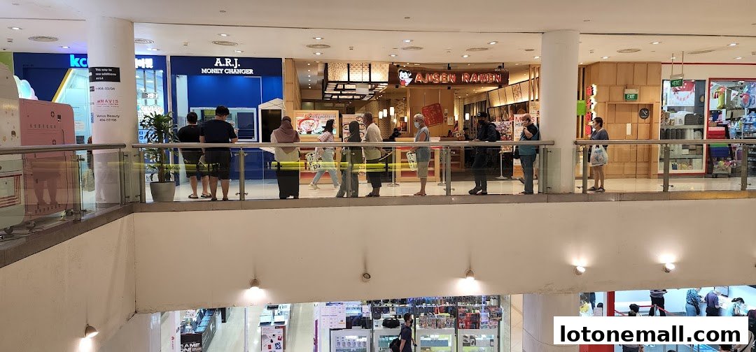 People queuing at A.R.J. Money Changer and Ajisen Ramen restaurants in a shopping mall.