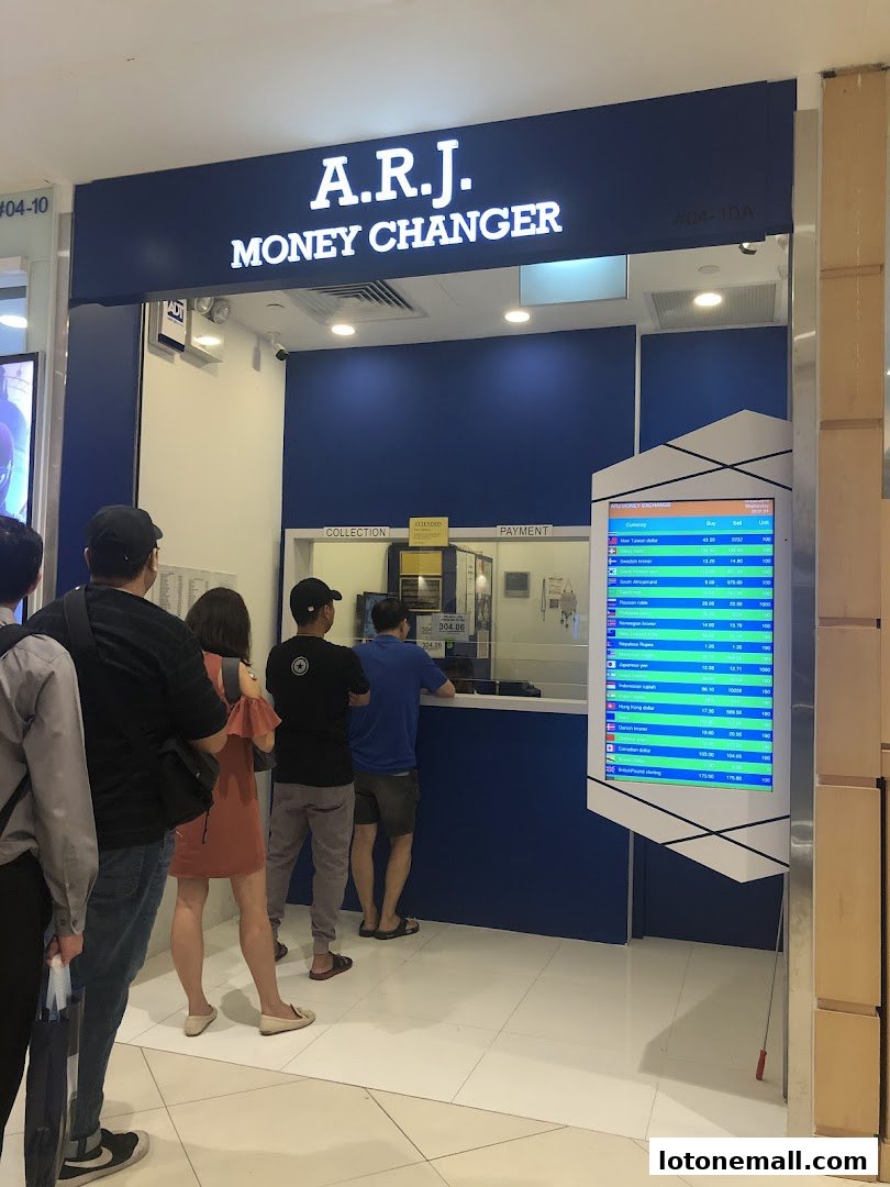 A.R.J. Money Changer shop with customers queuing and a digital display of exchange rates.