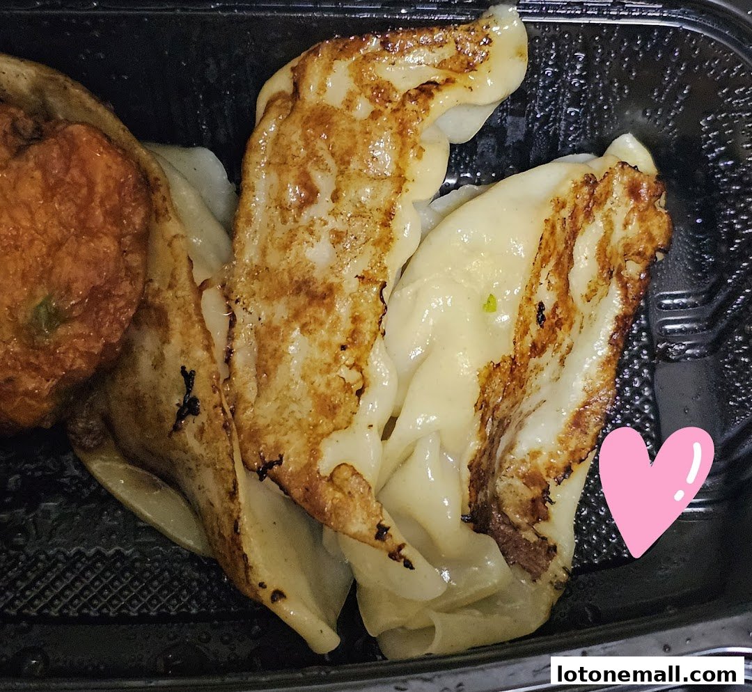 Close-up of pan-fried gyoza dumplings in a black takeout container.