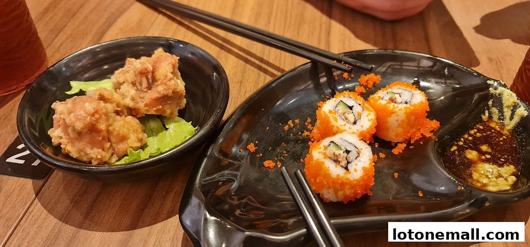 A close-up of Japanese food, featuring crispy fried chicken and California rolls with dipping sauce.