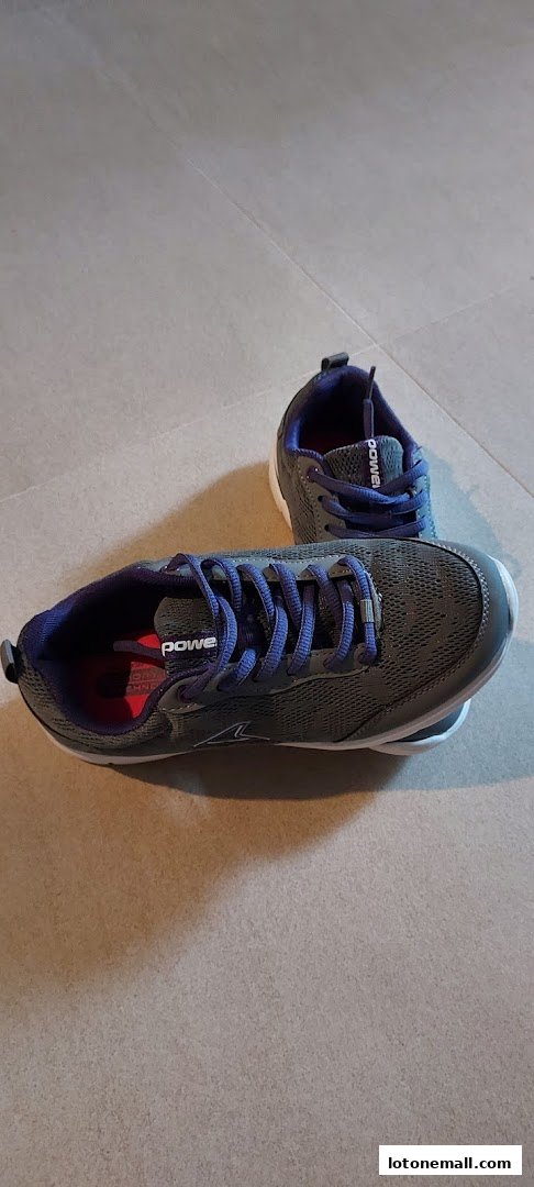 A pair of grey and purple athletic shoes with blue laces are displayed on a tiled floor.