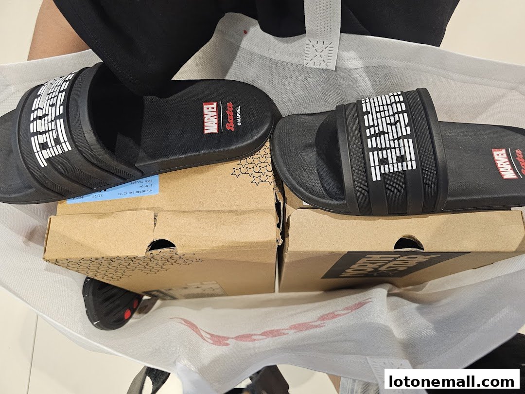 A pair of black Bata Marvel slides with boxes and a shopping bag.