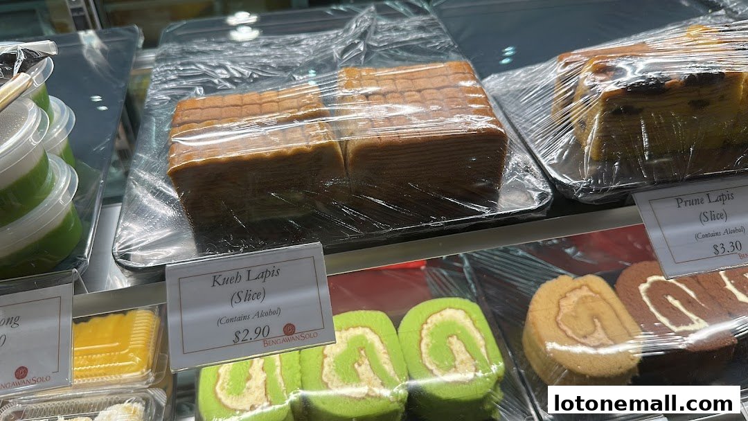 A display case filled with various layered cakes and swiss rolls, some individually wrapped.