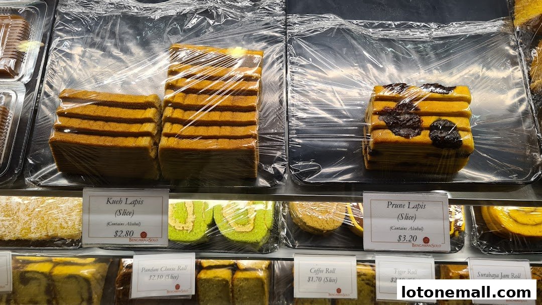 A display of various layered cakes and rolls, individually wrapped and labeled with prices.