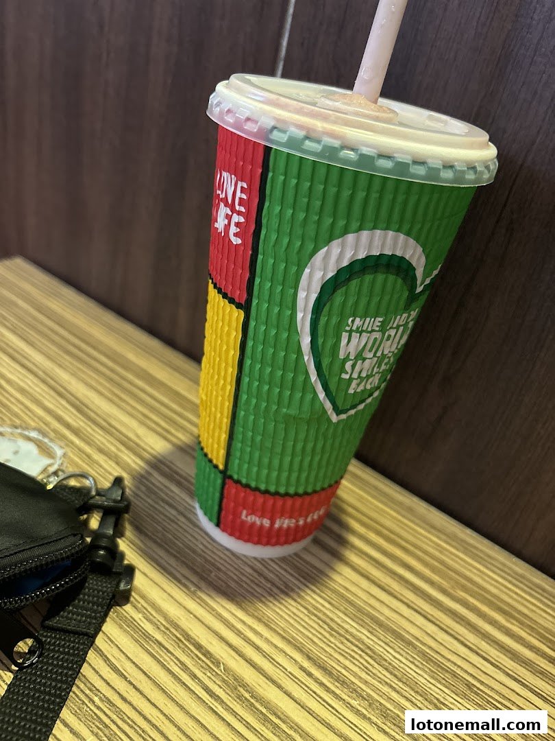 A colorful cup with a straw sits on a wooden table next to a black bag.