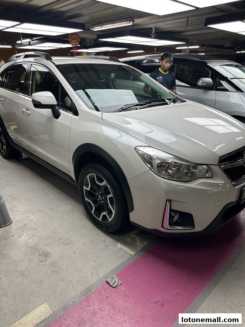 A white Subaru SUV is parked indoors, with a staff member standing nearby.