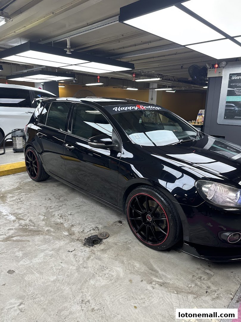 A black car with custom rims parked indoors, possibly at a car detailing shop.