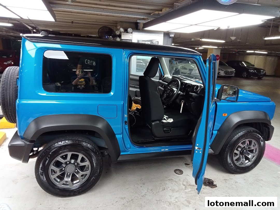 A bright blue Suzuki Jimny with the driver's door open, parked indoors.