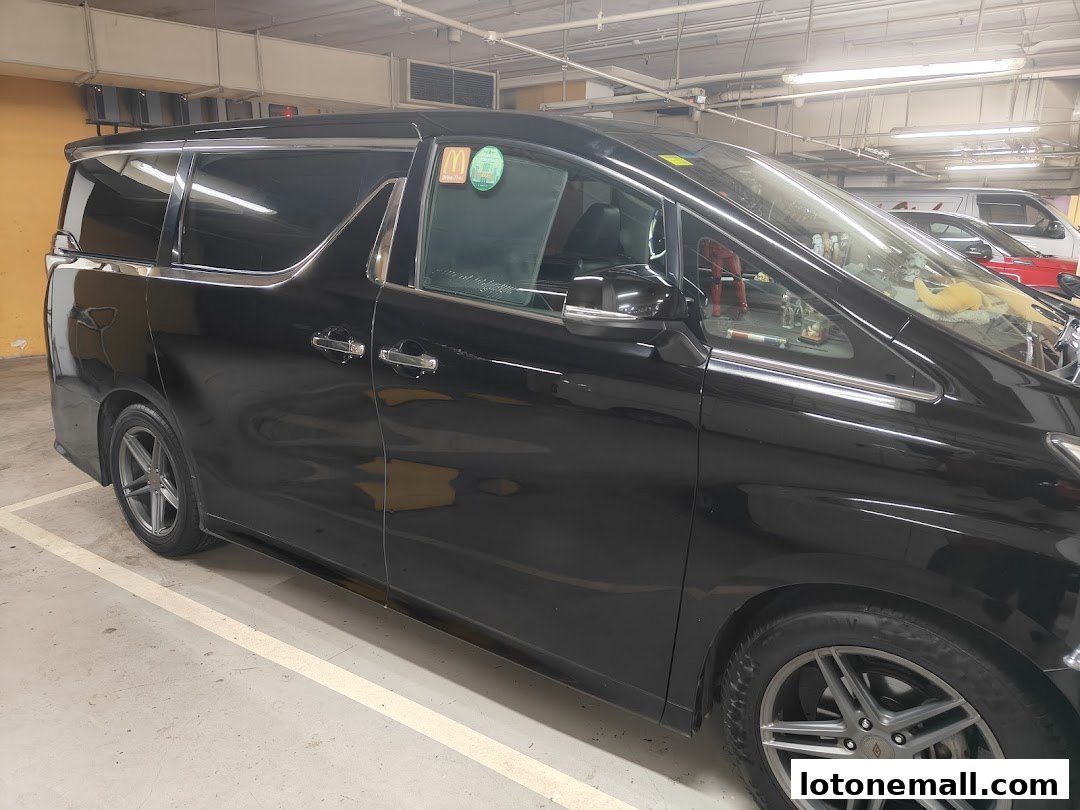 A black minivan parked in a parking lot with other vehicles visible in the background.