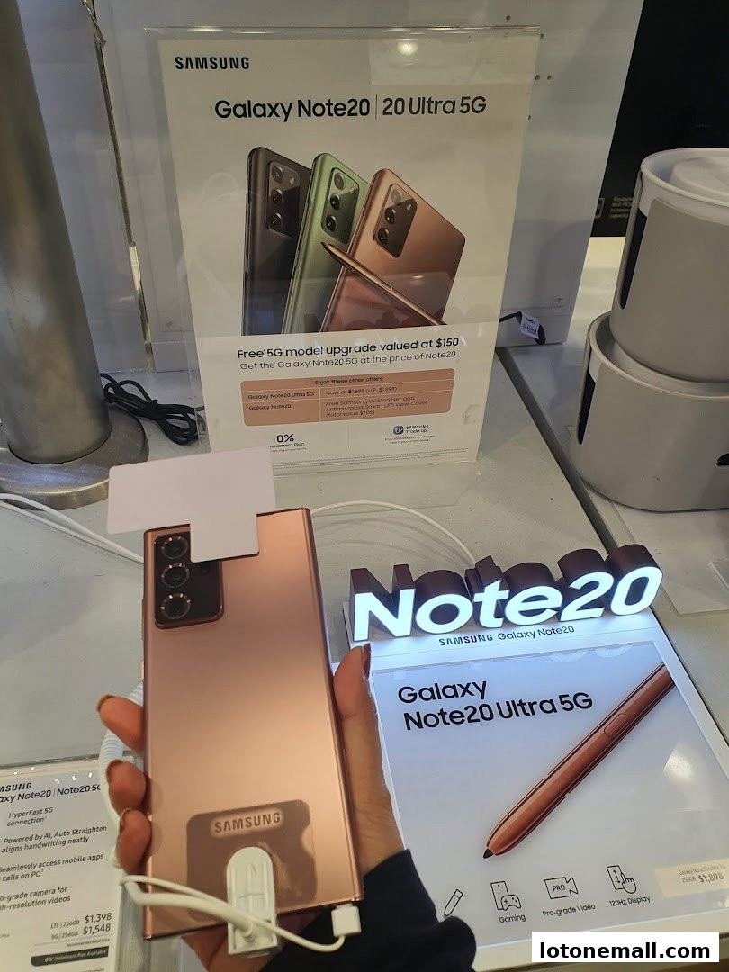 A person holds a rose gold Samsung Galaxy Note 20 Ultra 5G phone with promotional displays.