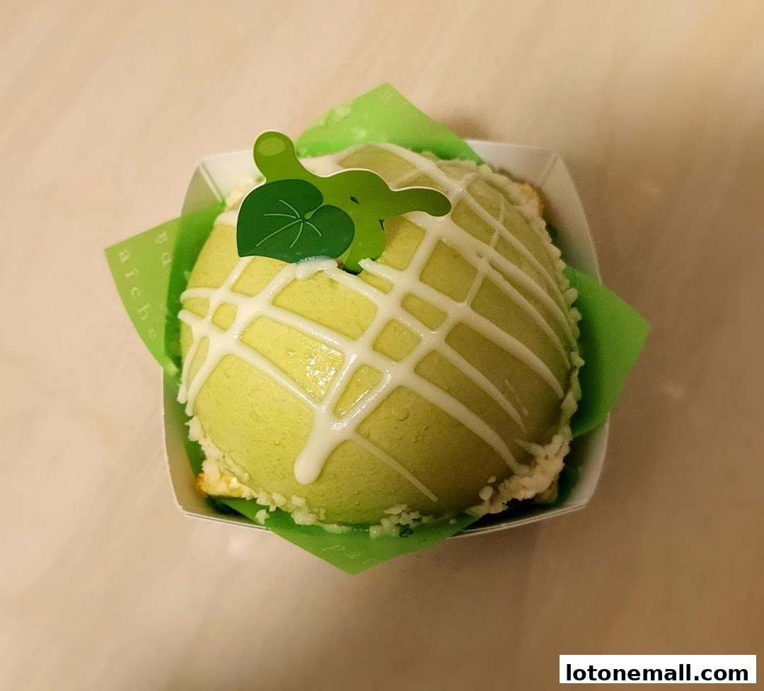 A close-up of a green, melon-shaped cake with white icing drizzle and a decorative leaf.