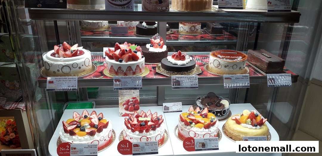 A display case filled with various beautifully decorated cakes, primarily featuring fresh strawberries and fruits.