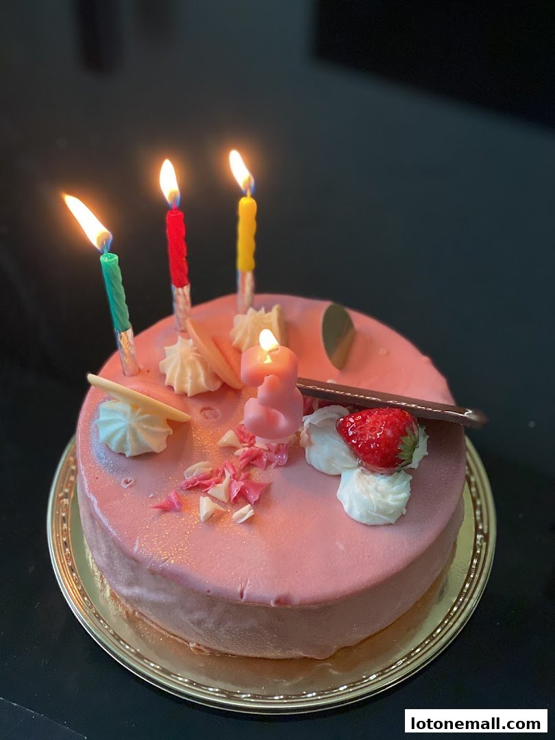 A pink frosted cake with lit candles, whipped cream, and a strawberry.