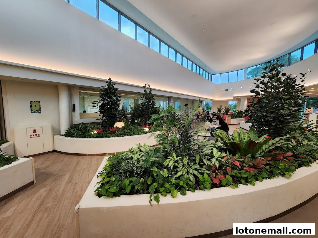 Interior of a library with lush greenery, seating areas, and large windows.