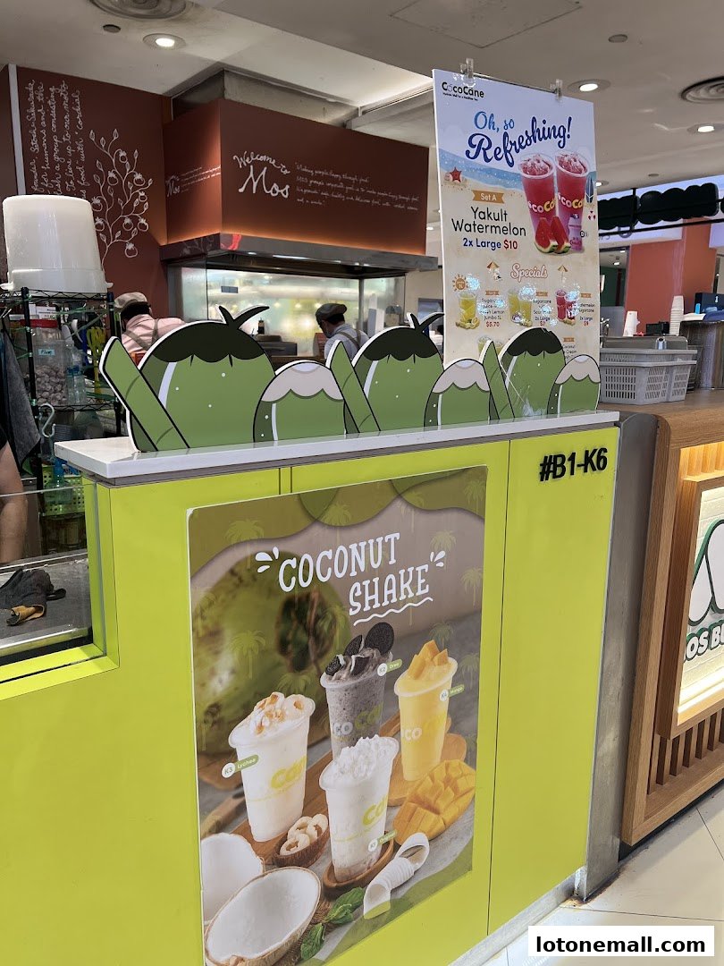 A bright yellow kiosk with a menu board advertising coconut shakes and Yakult Watermelon drinks.