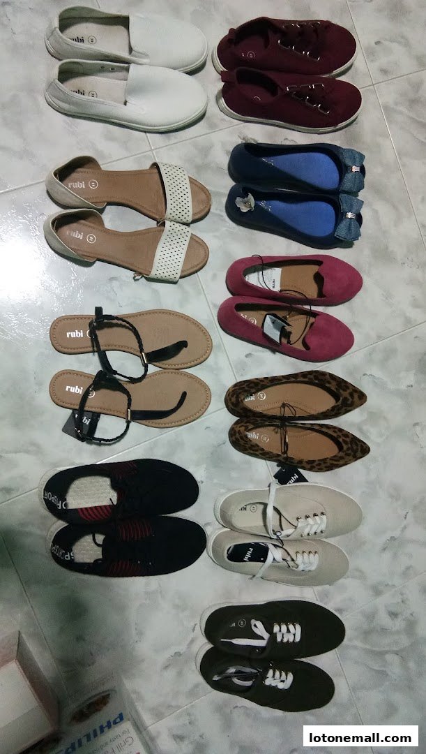 A collection of various women's shoes, including flats, sandals, and sneakers, neatly arranged on a tiled floor.