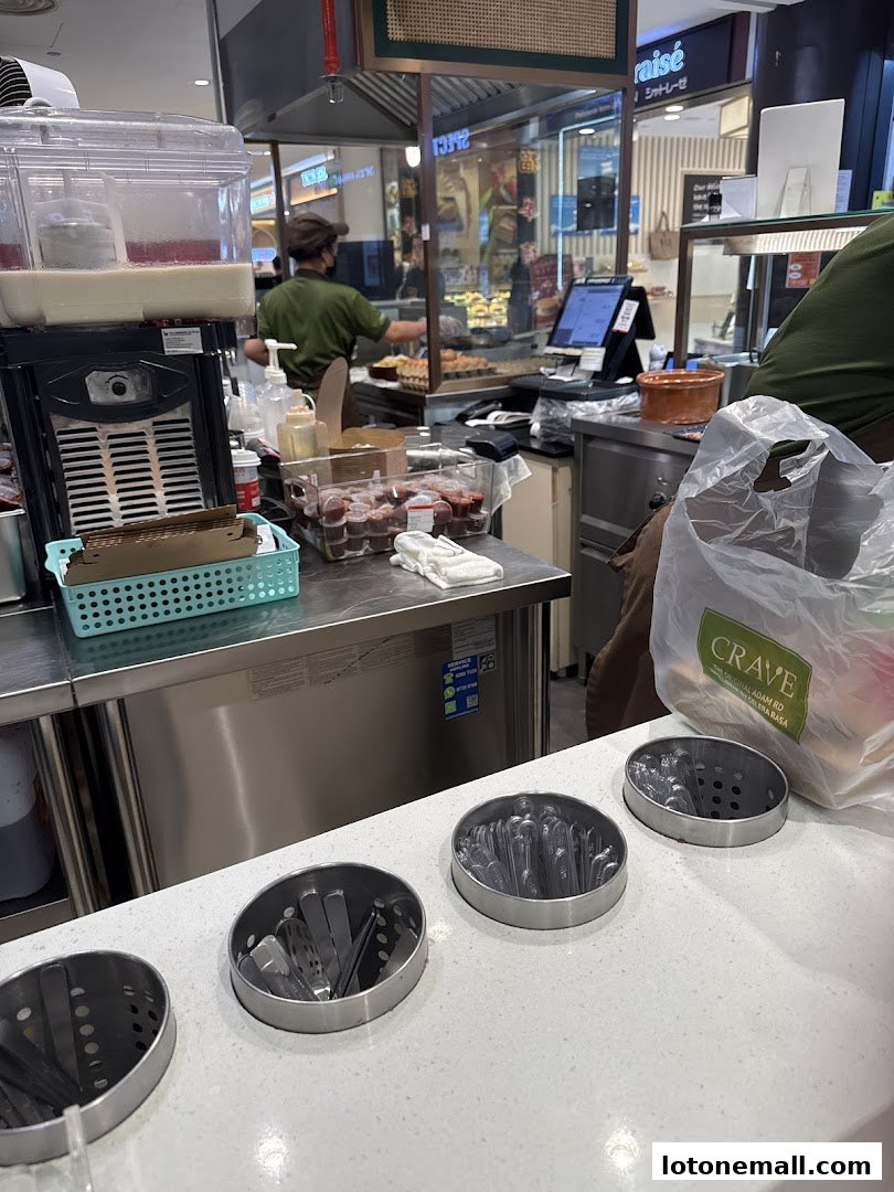 A food stall counter with cutlery holders and a staff member preparing food in the background.