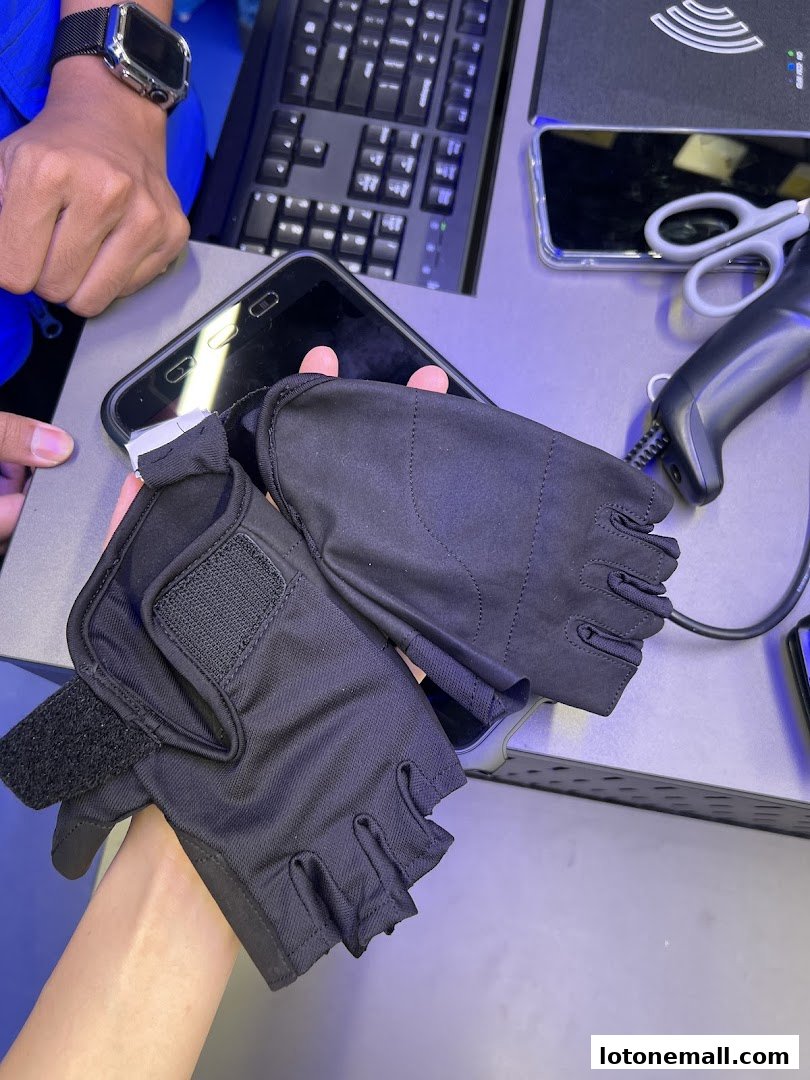 Hands holding black fingerless gloves over a smartphone with a keyboard and scanner in the background.