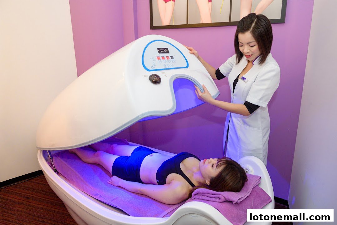 A woman lies in a slimming pod while a therapist adjusts the lid.