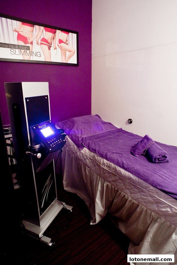 A treatment room with a slimming machine and a bed covered in purple towels.