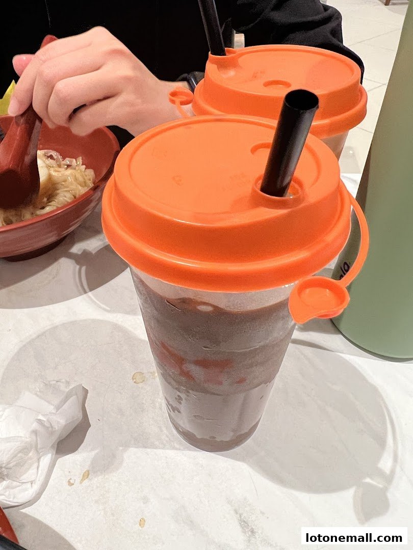 Two drinks with orange lids and straws, next to a bowl of noodles.