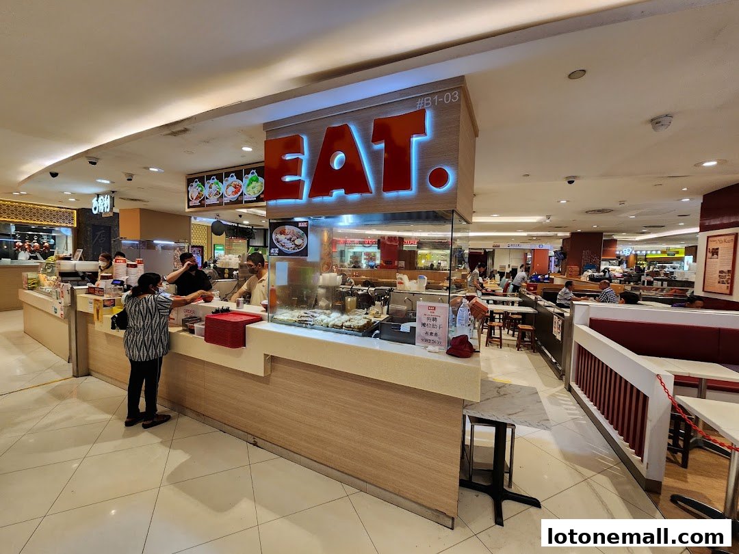 A food stall named EAT. Lot 1 with customers ordering and staff serving food.