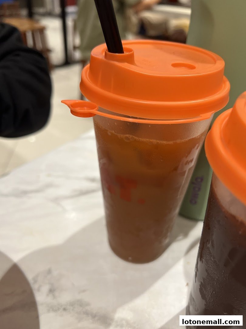 Close-up of two iced drinks with orange lids and straws on a marble table.