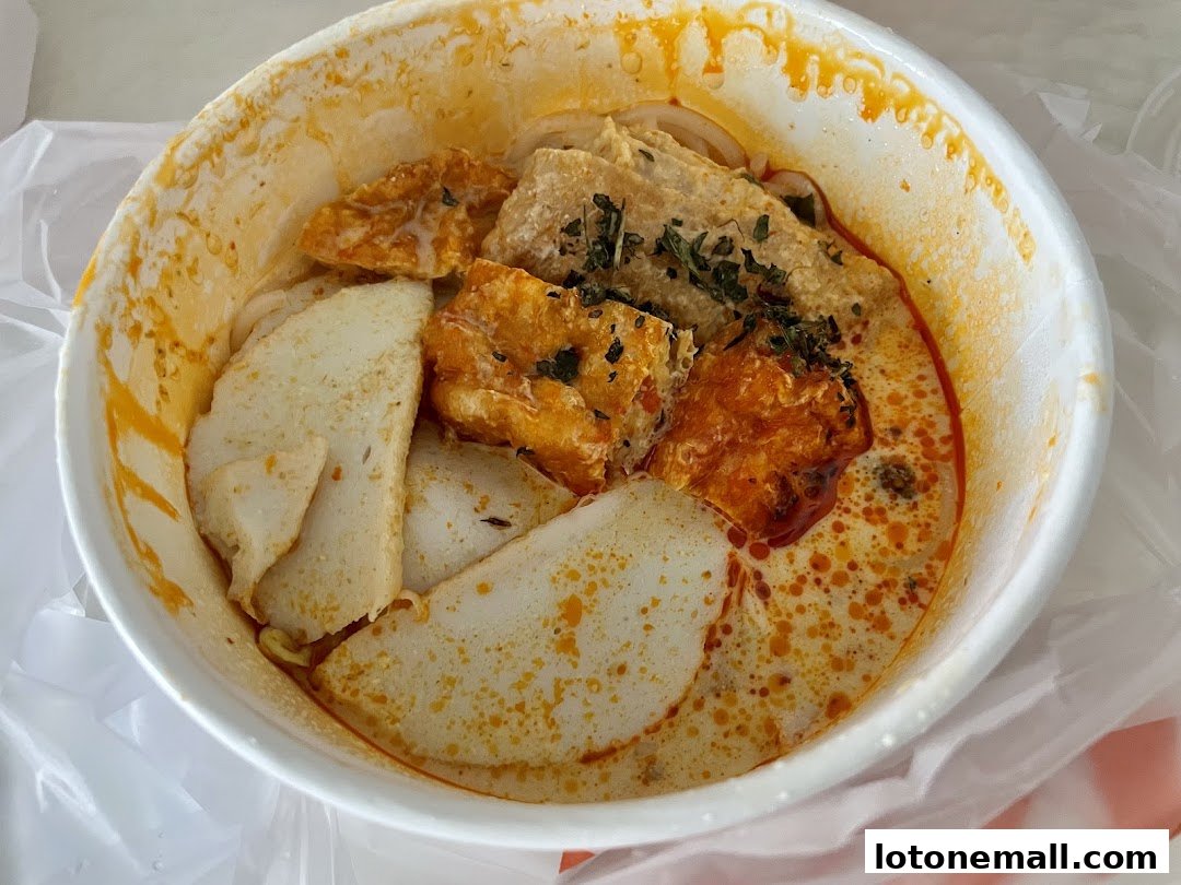 A close-up of a bowl of delicious curry laksa with fish cakes and fried tofu.