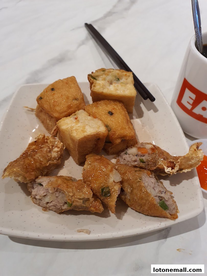 A plate of fried tofu and crispy spring rolls with chopsticks and a mug.