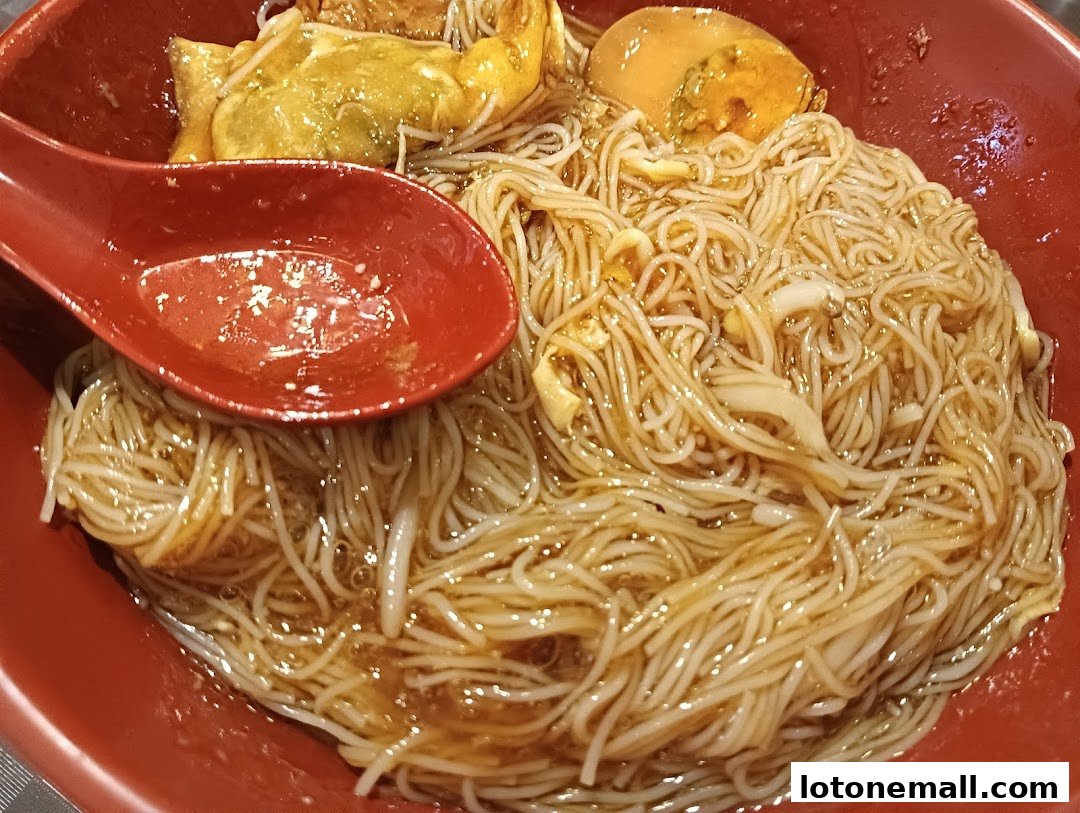 A close-up shot of a bowl of noodles with a red spoon and egg.