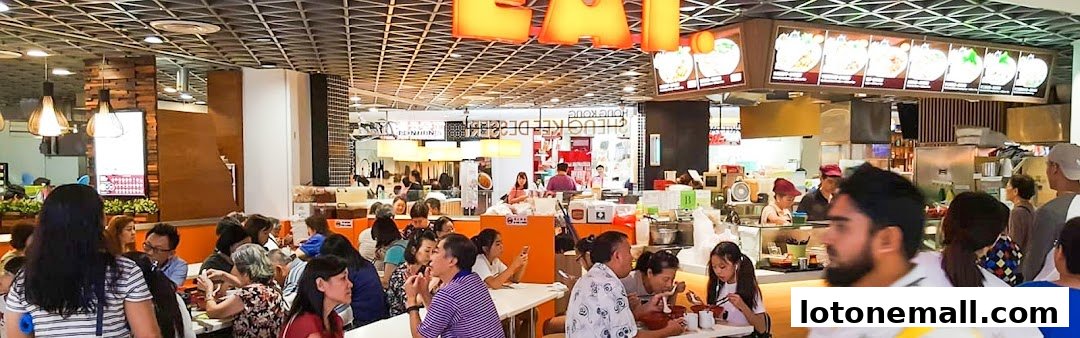 A busy food court with people eating and ordering at various stalls.