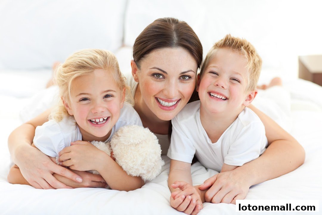 A mother and her two children are smiling and lying on a white bed.