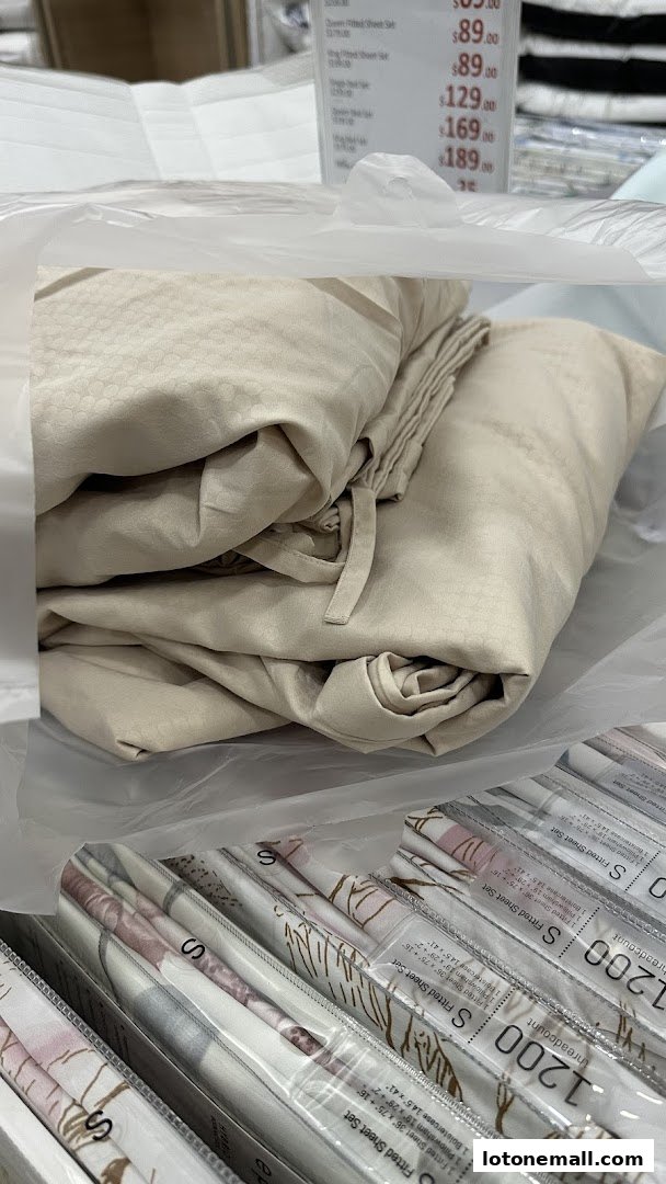 Close-up of folded beige bedding and packaged sheet sets with price tags visible.