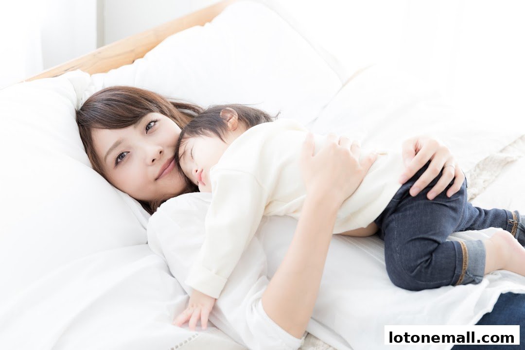 A mother lovingly holds her sleeping baby in bed, bathed in soft light.
