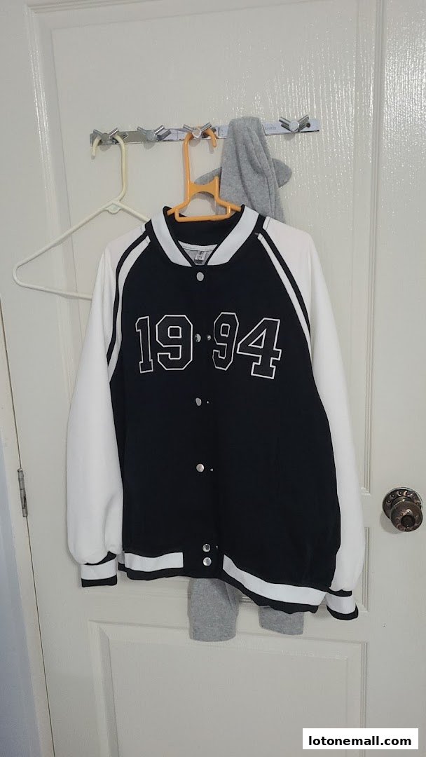 A black and white varsity jacket with '1994' printed on the front, hanging on a hook.