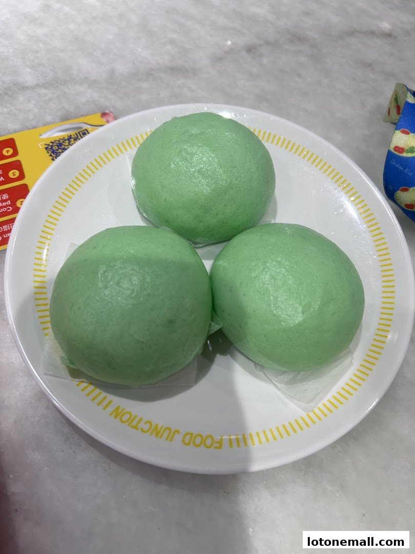 Three green steamed buns served on a white plate with yellow trim.