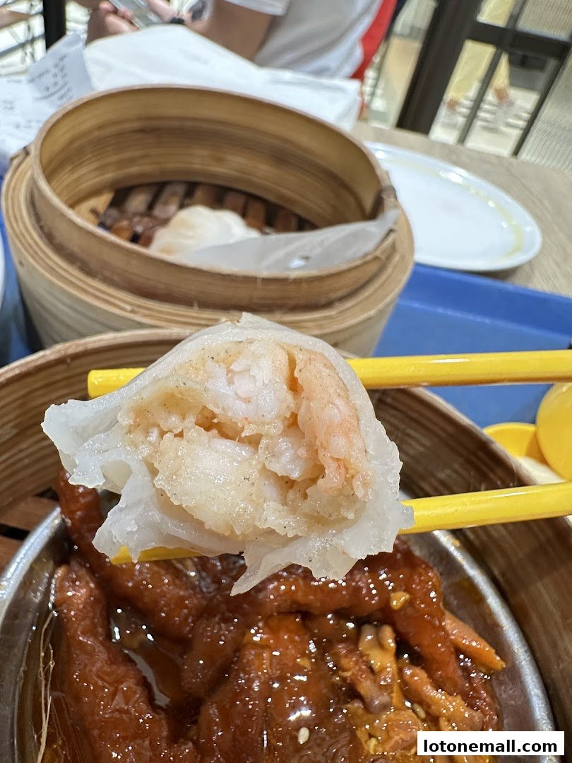 A close-up shot of delicious dim sum, featuring a shrimp dumpling held by chopsticks.