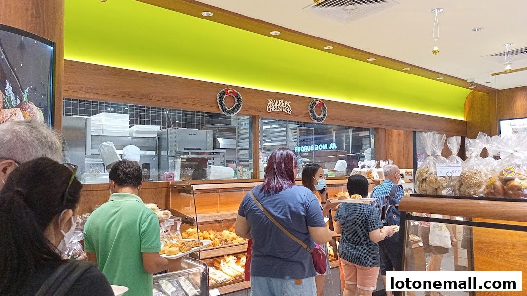 Customers queue inside a bakery with a display of fresh bread and pastries.