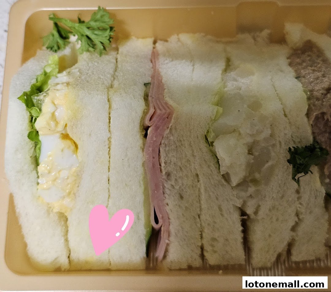 A close-up of a takeout container filled with assorted sandwiches, featuring egg salad and ham.