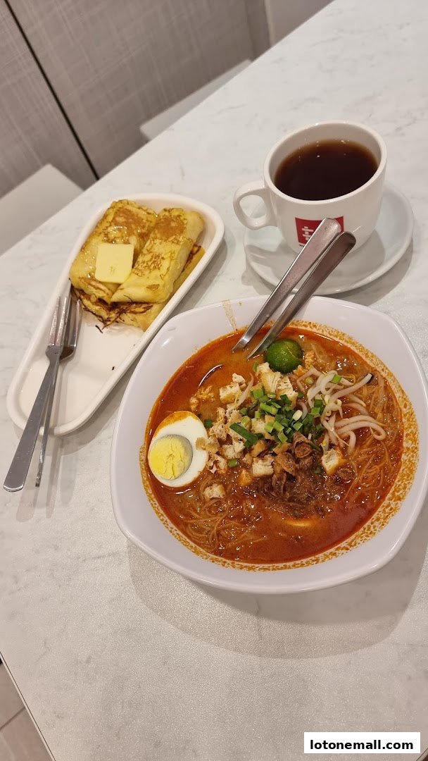 A bowl of curry noodles, French toast, and a cup of coffee on a marble table.
