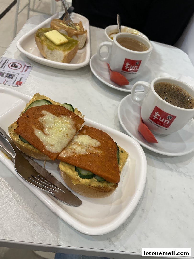 Two cups of coffee and two plates of food, including toast and a sandwich, are on a table.