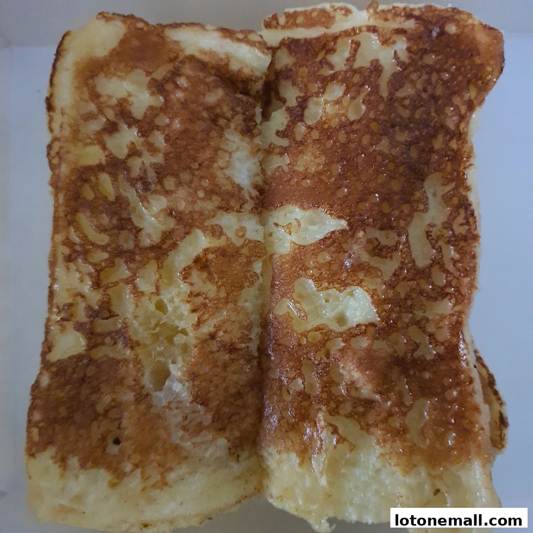 A close-up shot of two golden-brown slices of French toast, glistening with syrup.