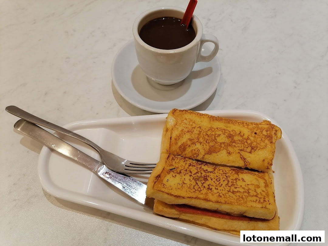 A serving of French toast with a cup of coffee and cutlery on a white table.