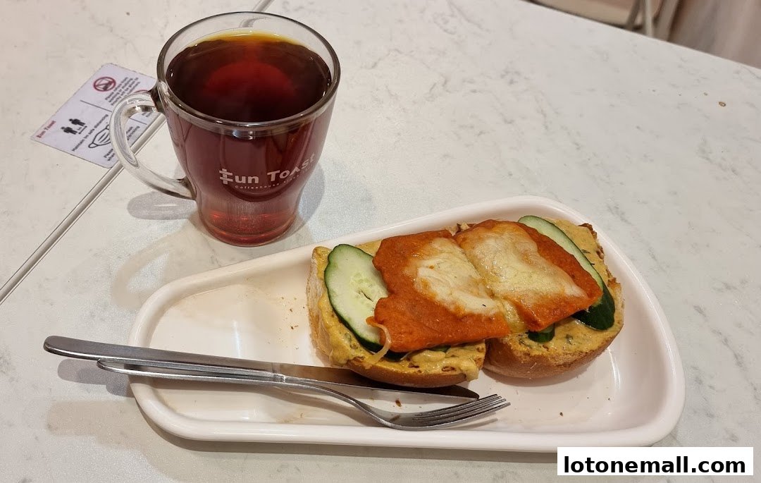 A cup of tea and a half-eaten sandwich with cheese and cucumber on a white plate.