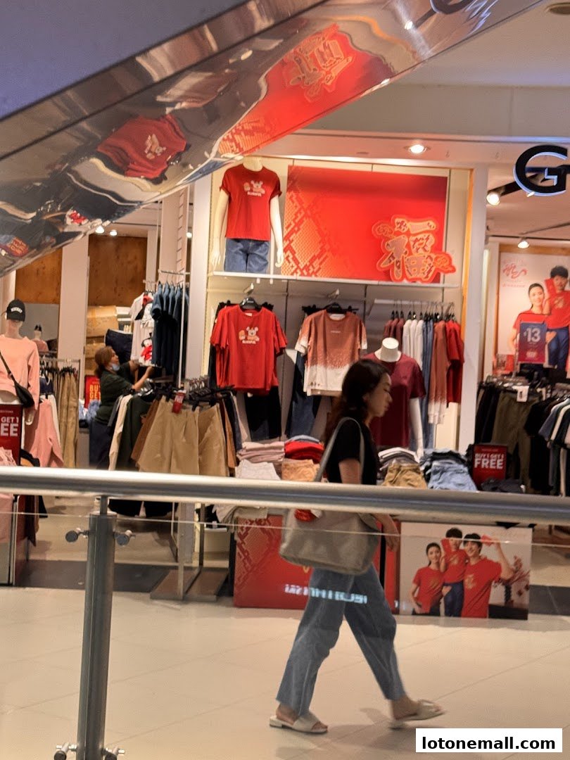 A woman walks past a Giordano clothing store display featuring red apparel and mannequins.