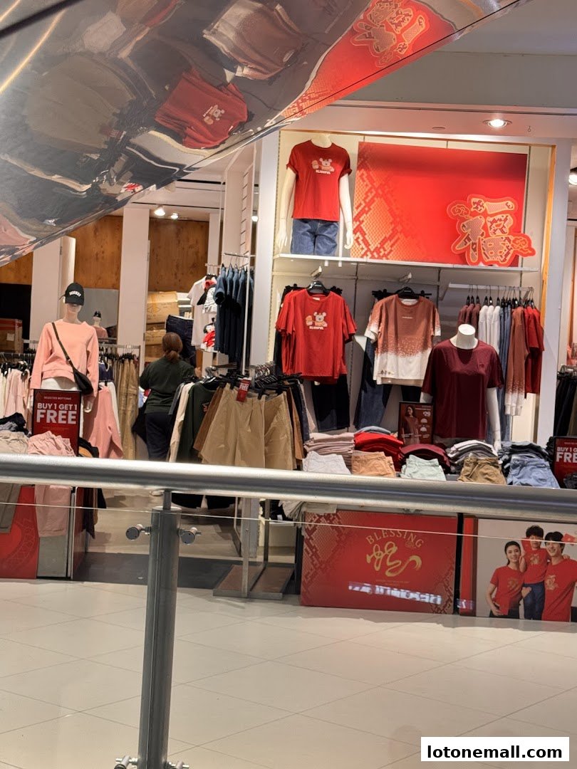 A clothing store interior with mannequins and racks of apparel, featuring red promotional signage.