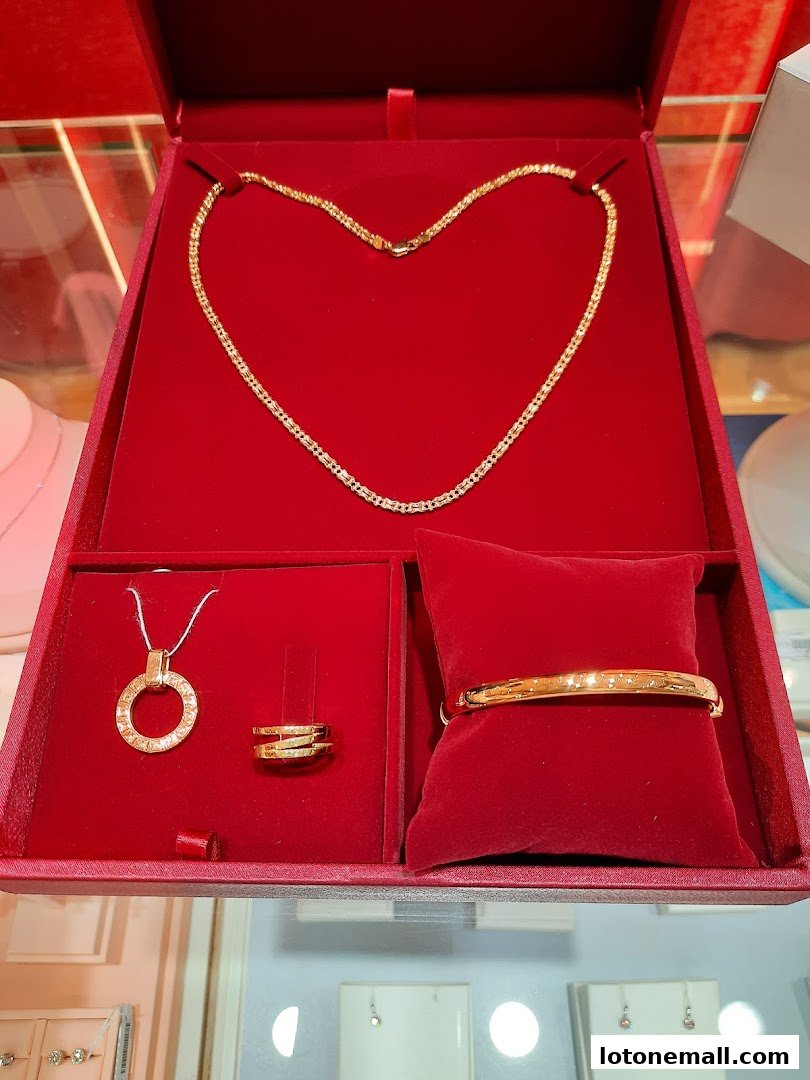 A red jewelry box displaying a gold necklace, pendant, ring, and bracelet.