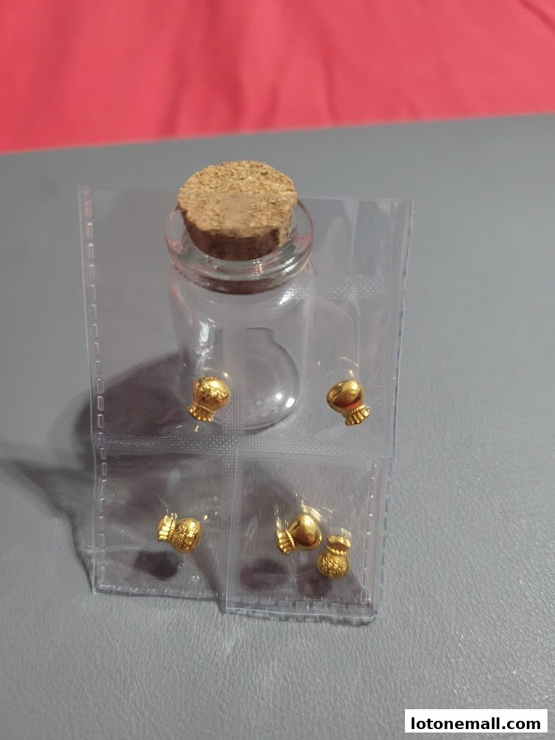 Small gold charms in the shape of traditional Chinese motifs displayed in a clear bottle.