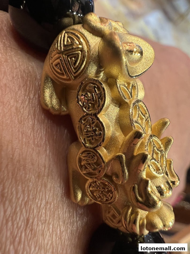 Close-up of a gold bracelet with intricate carvings and black beads.
